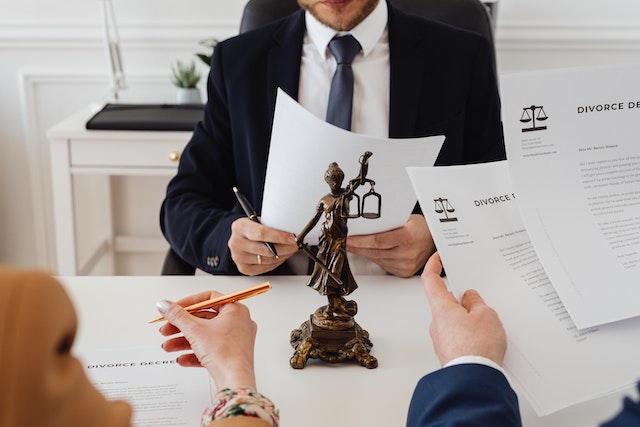 lawyer discussing a divorce with a couple, a statue of Lady Justice and her scales sits at the desk