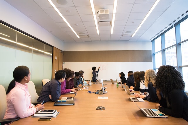 office meeting held in a large conference room with a woman presenting at a whiteboard