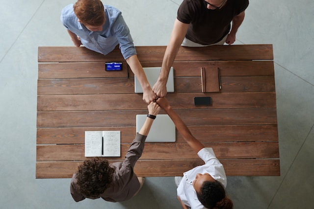 birds eye perspective of four colleagues fist bumping at a work desk