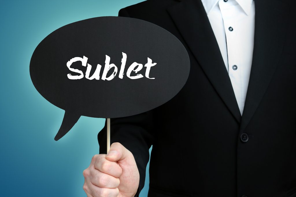 man in a suit holding a small sign that reads Sublet