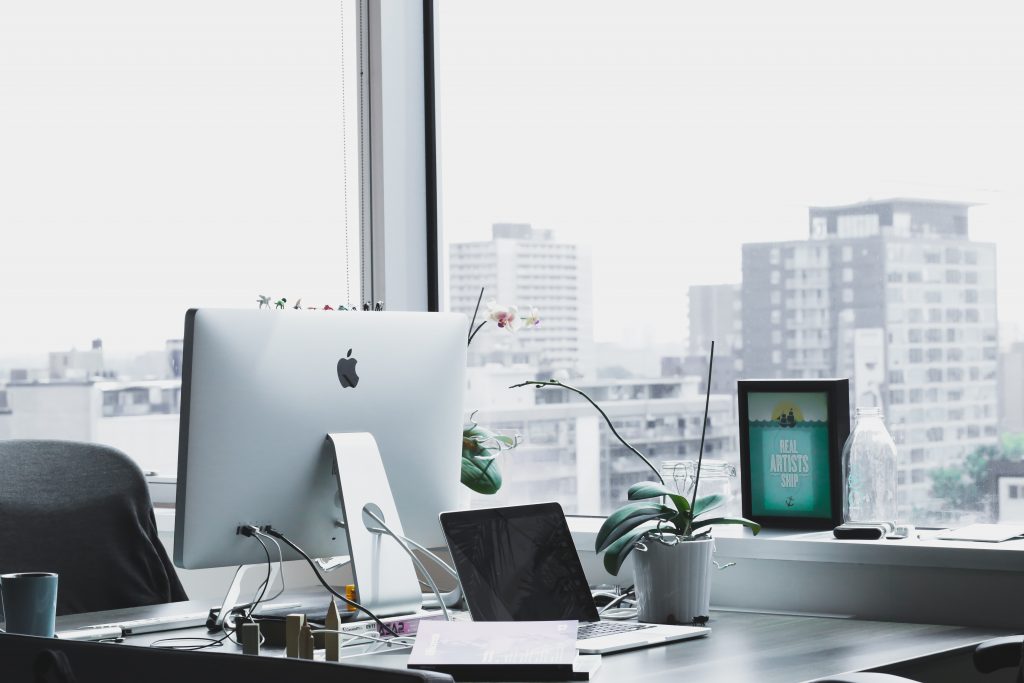 Mac computer sitting on a desk with a cityscape behind it