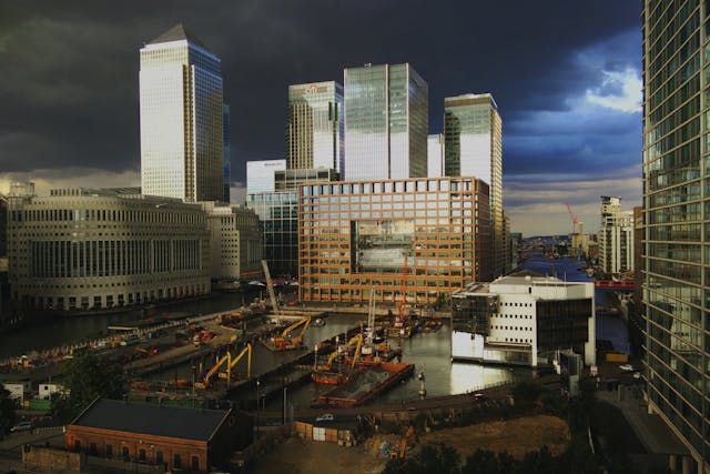 A view from the centre of Canary Wharf looking towards construction occurring across one of the area’s many waterways, with shiny high-rises forming the skyline in the background. Image at LondonOfficeSpace.com.