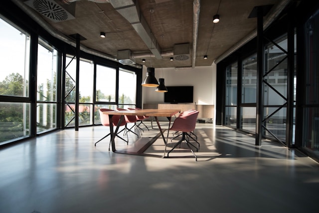 View from one end of a cavernous modern Fitzrovia boardroom with a long meeting table and chairs running down the centre. Floor-to-ceiling windows cover the full left side of the room, granting views of trees in daylight. Image at LondonOfficeSpace.com.