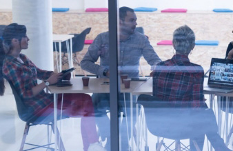 three colleagues sitting down and meeting at a table behind glass