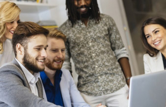 five colleagues smiling and pointing at a laptop during a meeting 